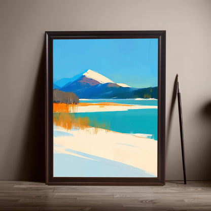 A large, dark wood-framed art print of a snowy mountain and turquoise lake leaning against a neutral-colored wall on a light wooden floor. A single artist's paintbrush leans against the wall beside the frame.