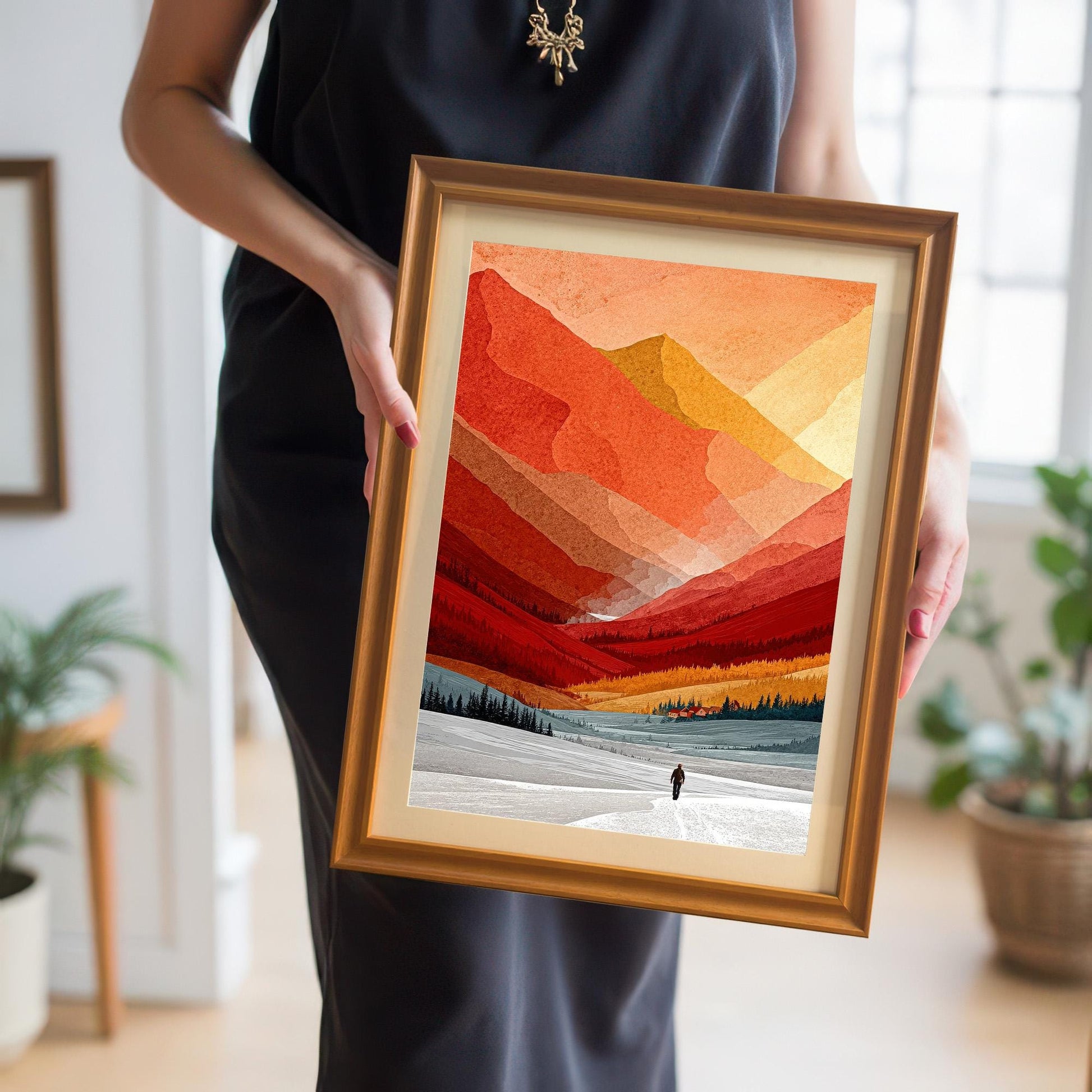 A person holding the framed mountain landscape print to show the physical scale and quality of the orange-toned wood frame and matting.