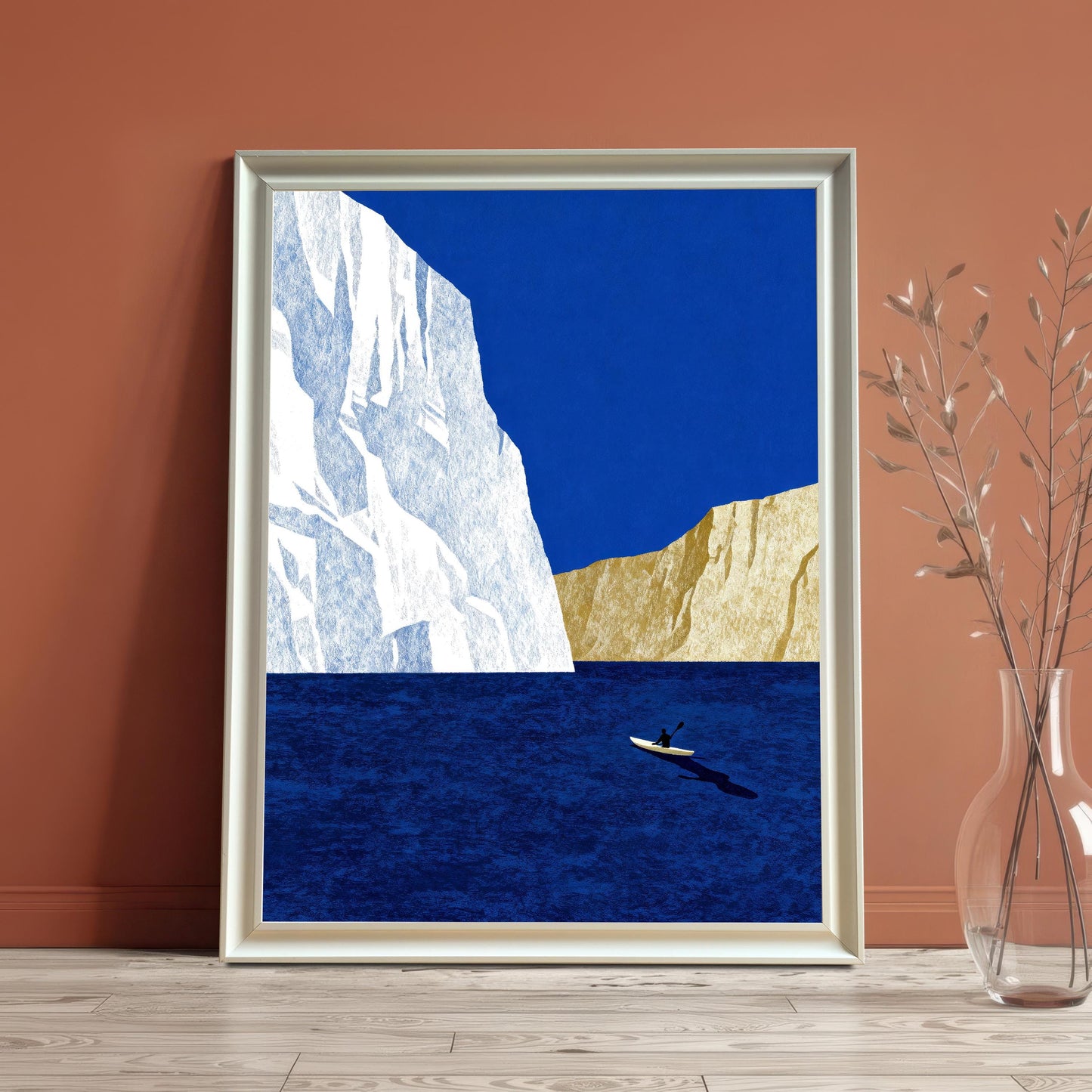 Modern nautical art print with a white wood frame, leaning against a terracotta-colored wall next to a glass vase with dried branches.