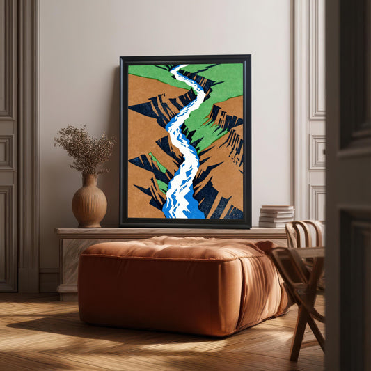 A large, modern black-framed art print featuring an abstract canyon and river landscape, displayed as a focal piece on a wooden console table in a minimalist, sunlit room.