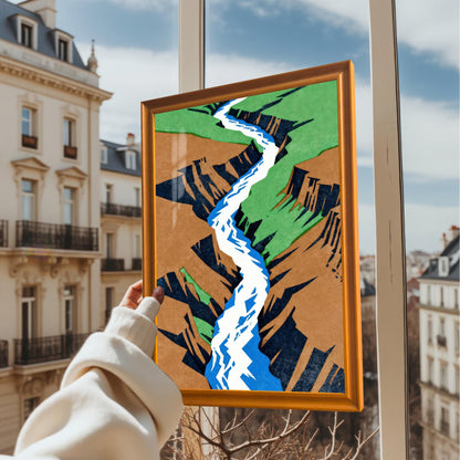 A person holding the orange-framed canyon art print in front of a window with a blurred Parisian city street background, showcasing the frame's finish in natural light.