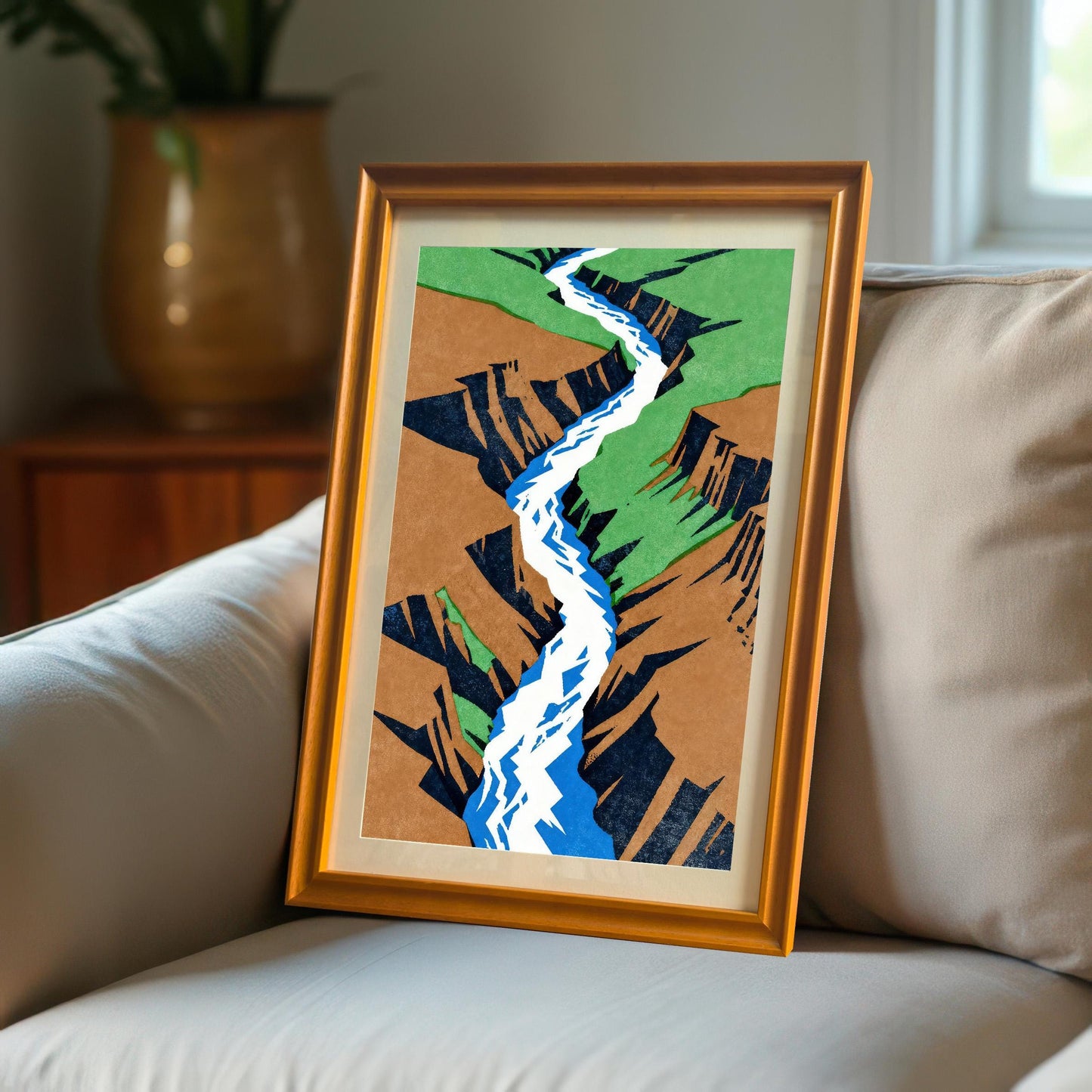 The orange-framed art print leaning against a soft grey sofa cushion in a cozy living room setting, demonstrating its use as versatile home decor.