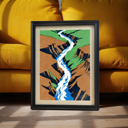 A black-framed landscape art print with a cream mount, leaning against a vibrant mustard yellow sofa on a light wood floor, captured in warm, natural sunlight.