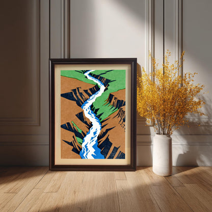 A dark coffee-colored wood frame with a cream mount, showcasing the colorful canyon art as it sits on the floor next to a tall vase of bright yellow wildflowers in a sophisticated, sun-drenched room.