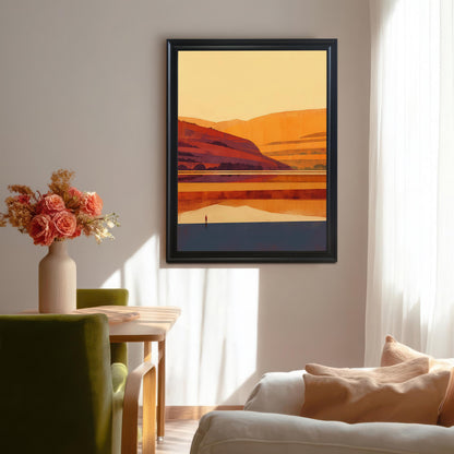 A black wood-framed sunset landscape art print hung on a neutral wall in a sunlit dining area with a green velvet chair and floral vase.