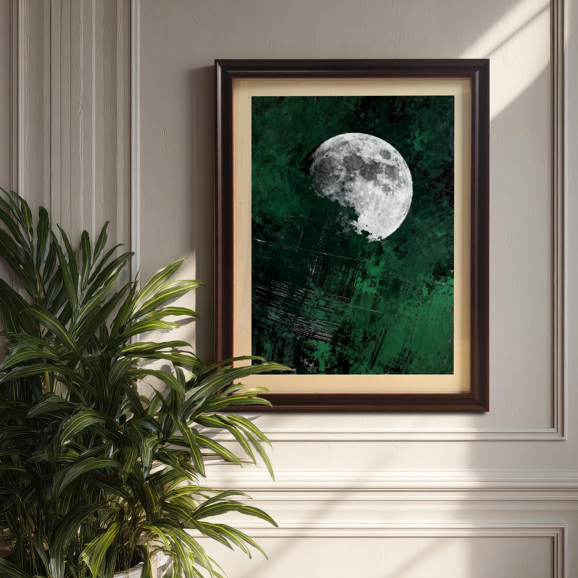 Dark coffee-colored wood frame with a matted moon print hung on a classic wainscoted wall next to a large green indoor plant.