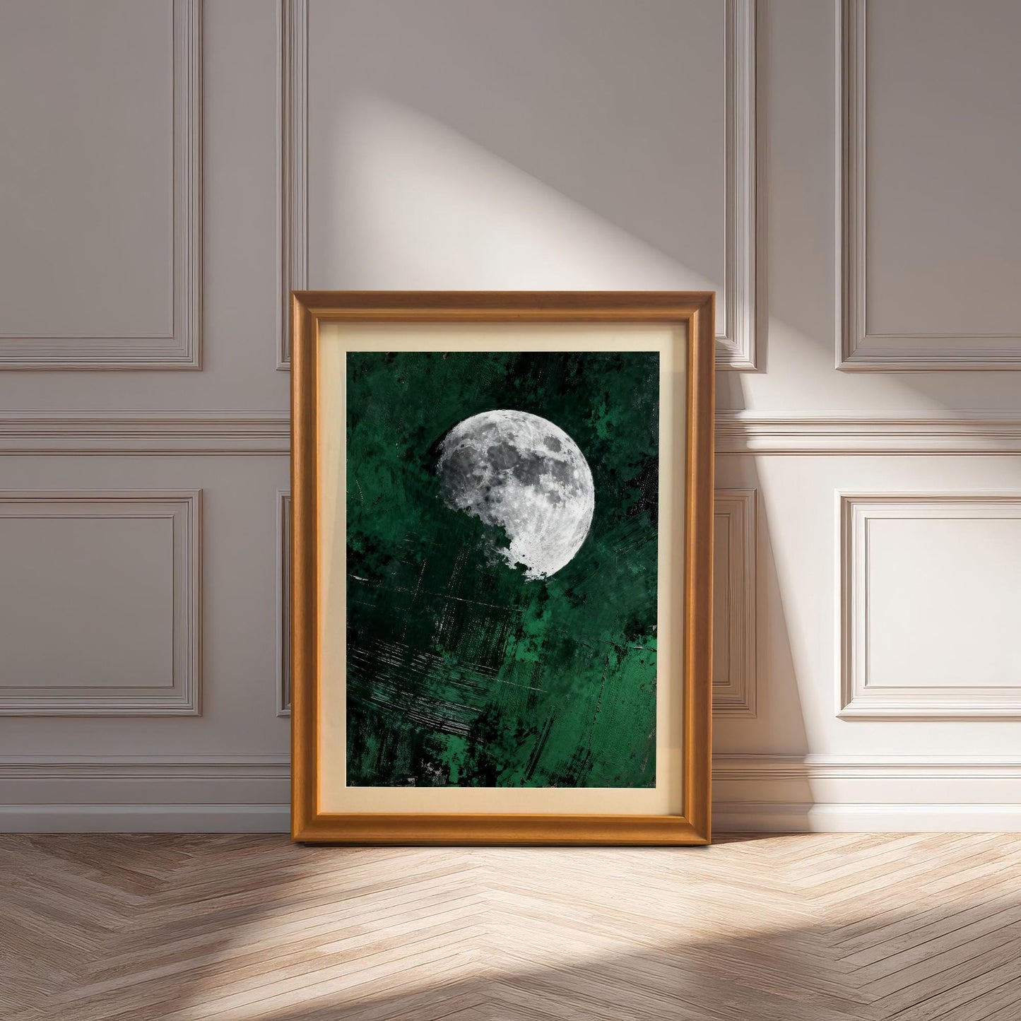 An orange-toned wood frame with a matted moon art print leaning against a white paneled wall on a light wood herringbone floor.