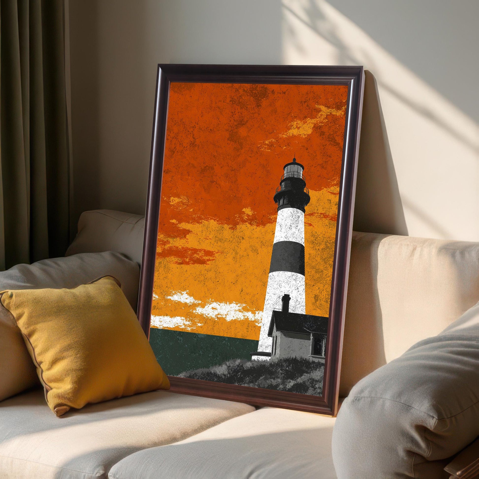 A framed lighthouse art print in a dark coffee wood frame leaning on a beige sofa next to a yellow pillow, showing natural window light and shadows.