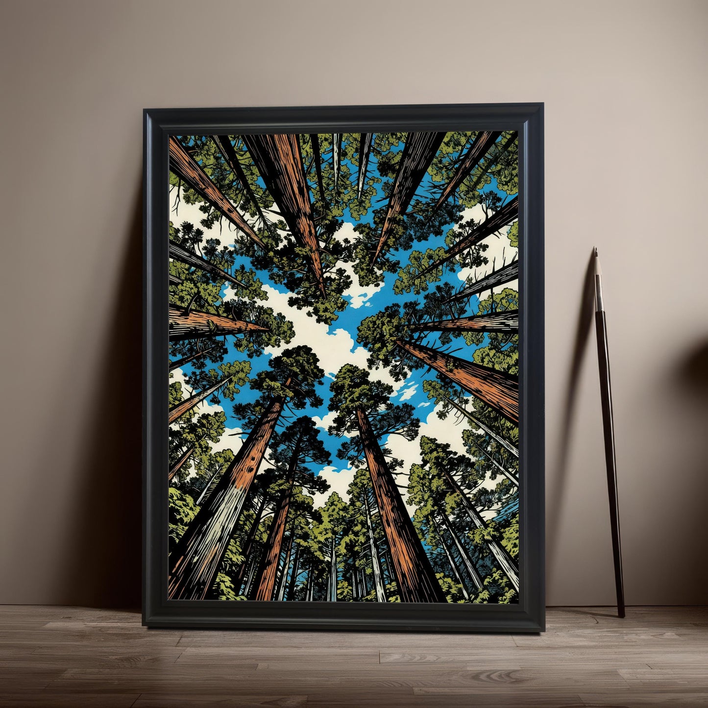 Vertical black wood framed wall art featuring a towering sequoia forest illustration from a worm's-eye view against a blue sky, leaning against a neutral wall.