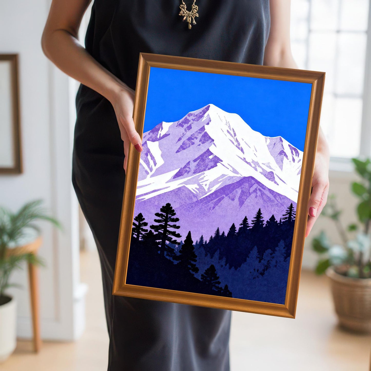 A person in a black dress holding the mountain art print in a gold-colored 'Orange' wood frame, showing the scale and vibrant colors.