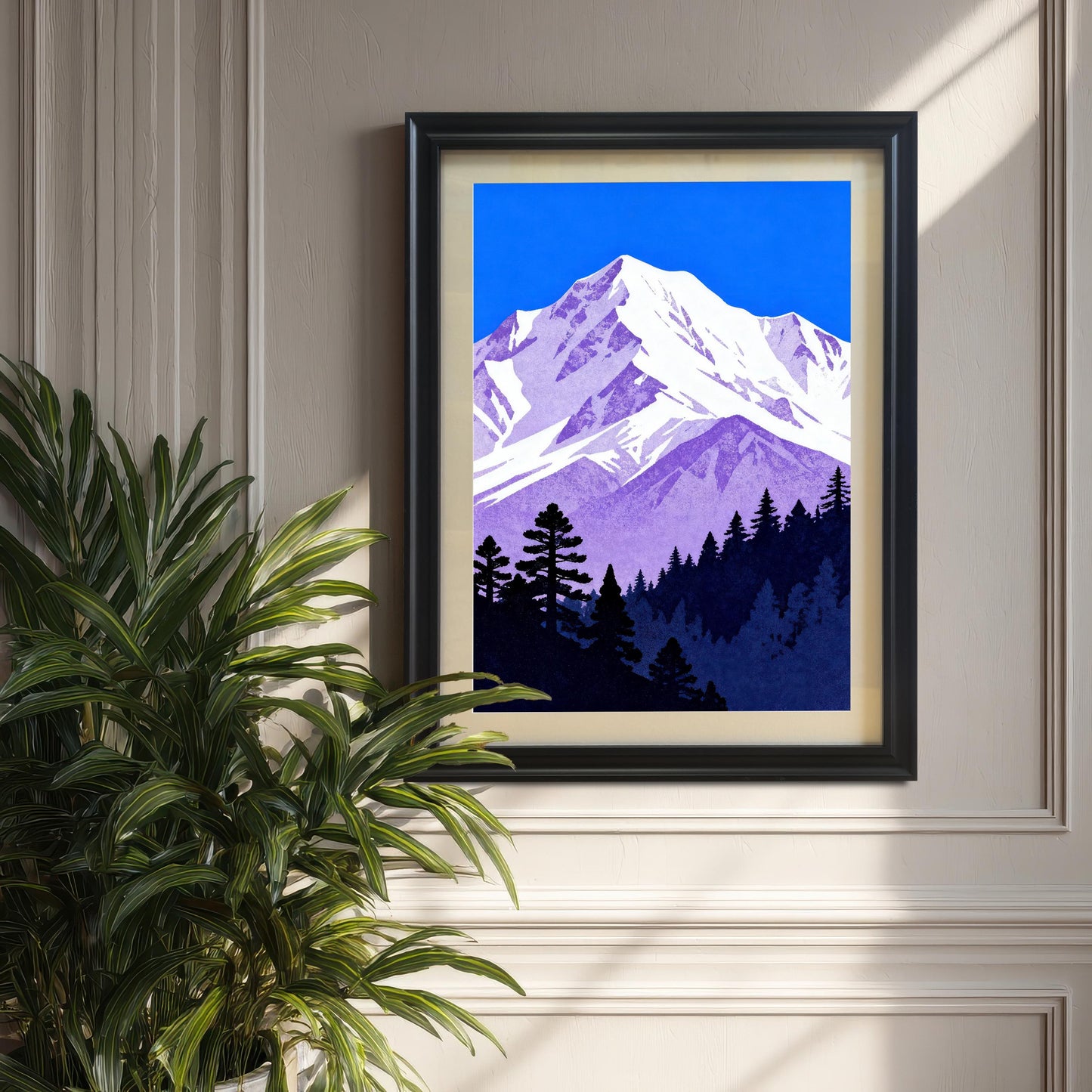 The purple and blue mountain art print in a 'Black' wood frame with a cream mount, displayed on a textured wall next to a large potted plant.
