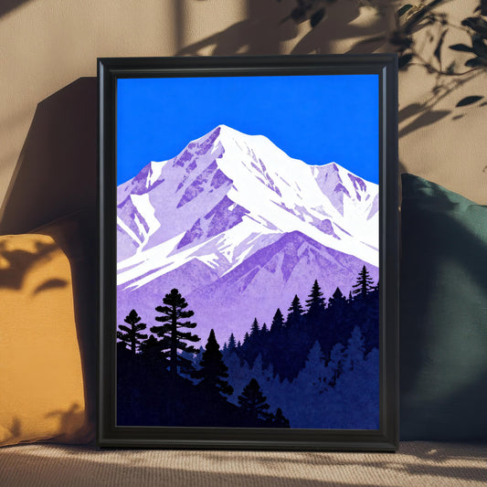 The purple and blue mountain art print in a 'Black' wood frame, leaning against accent pillows on a couch or chair, showcasing shadows and natural light.