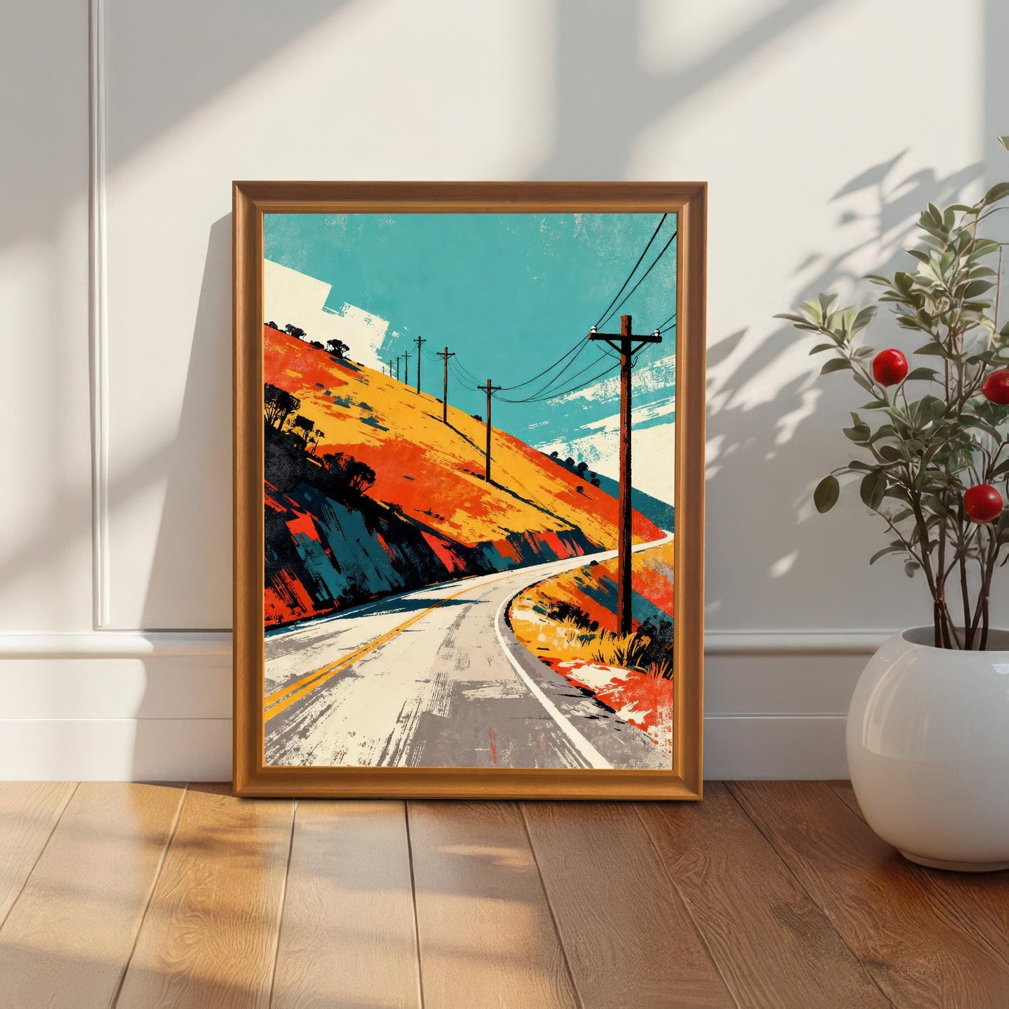 Framed art print in an Orange or light wood frame, leaning against a white wall next to a white planter with a small red-berried plant. Natural sunlight creates a dramatic diagonal shadow across the wall and print.