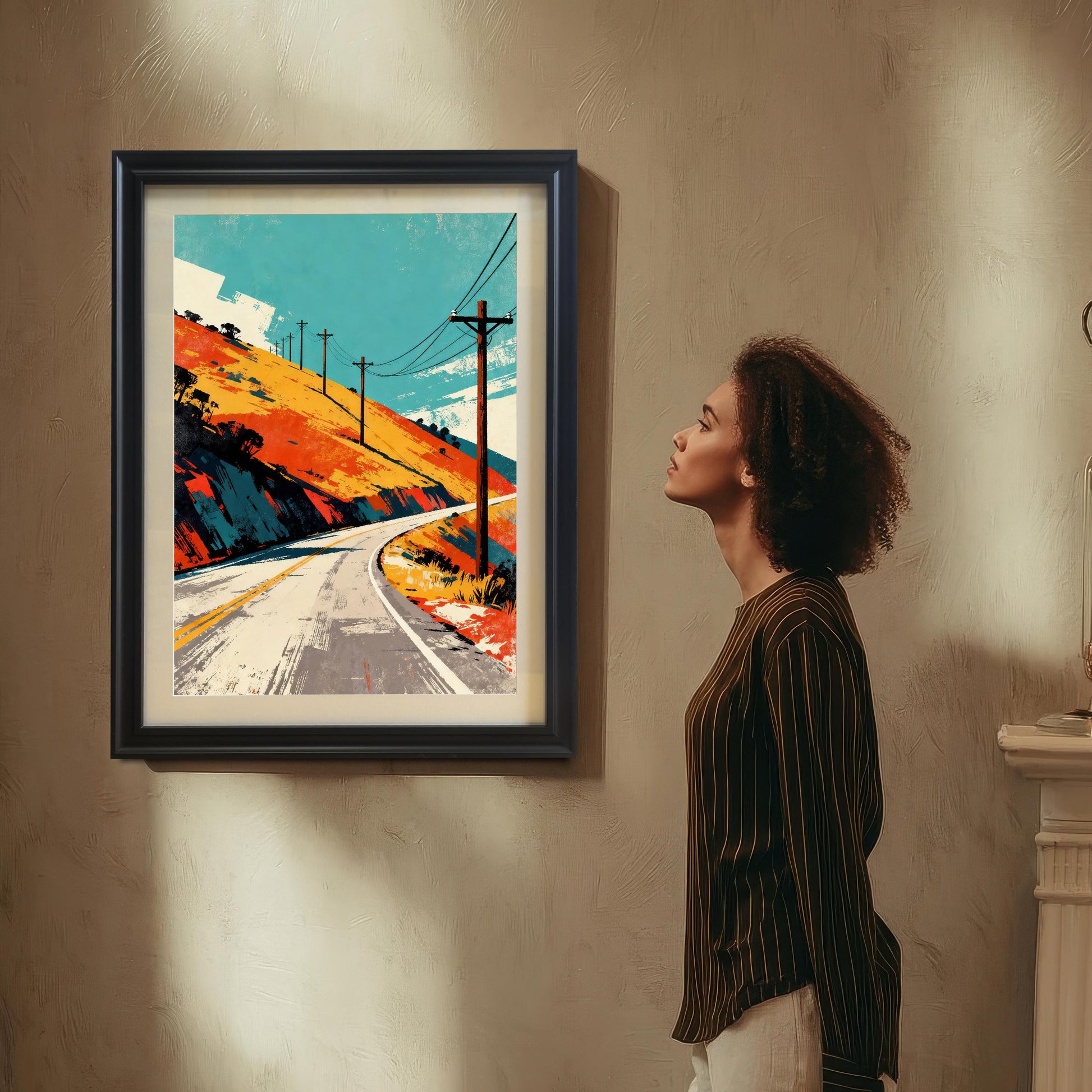 A woman with curly hair, wearing a striped brown shirt, stands to the right of the framed art print, looking up at it. The print, in a Black Frame with a white mount, is hung on a textured beige wall.