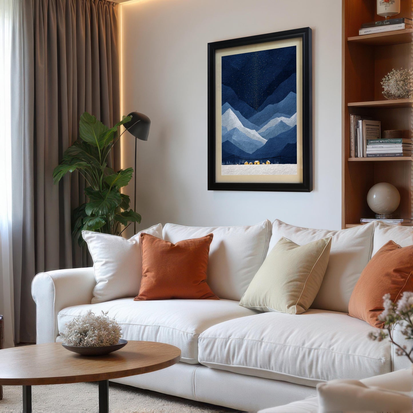 A modern living room featuring a white sofa with orange and cream pillows, with a large black-framed mountain art print hanging on the wall above it.
