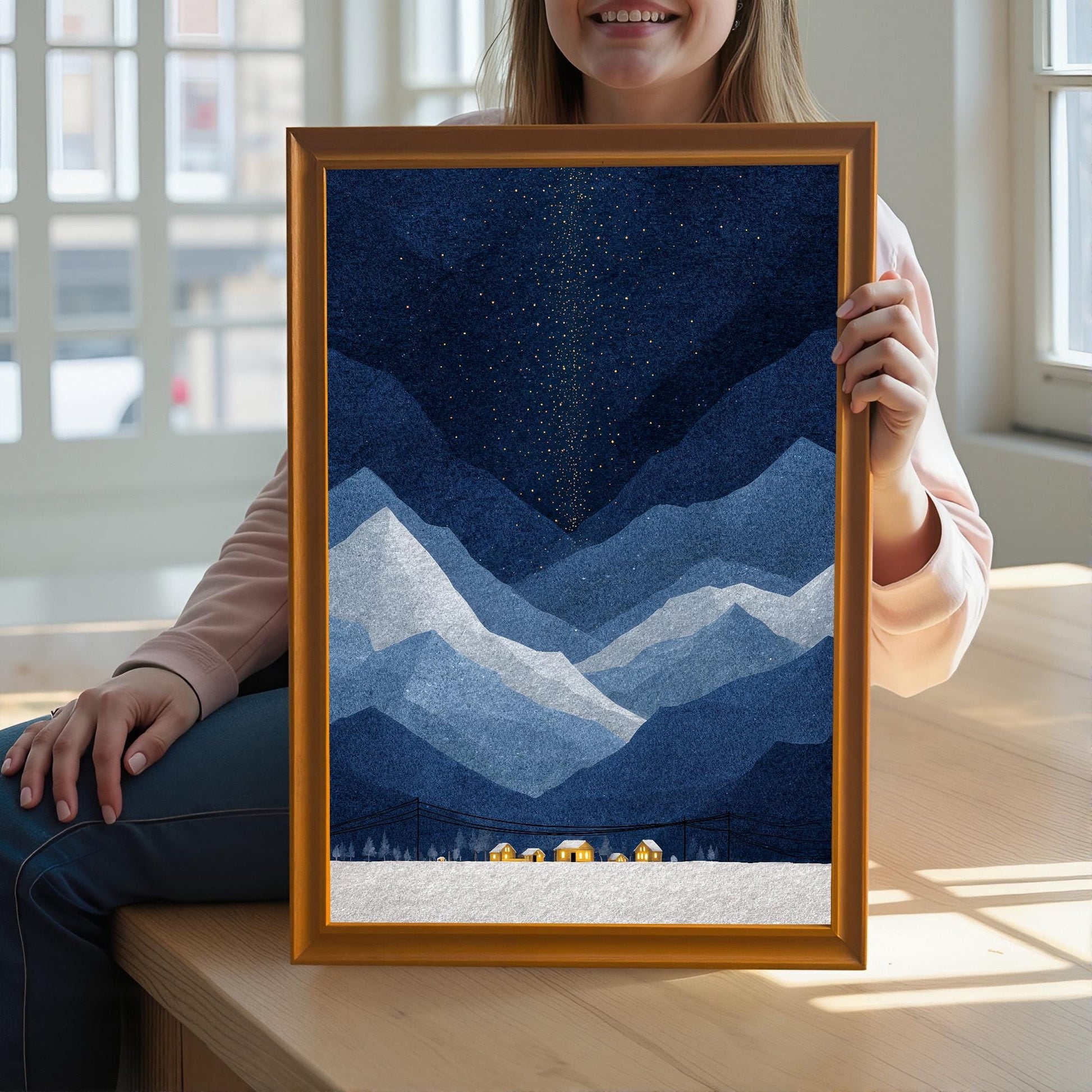 A woman holding a large, orange-wood framed art print of a starry night over blue mountains, showcasing the scale of the artwork against a bright, indoor background.