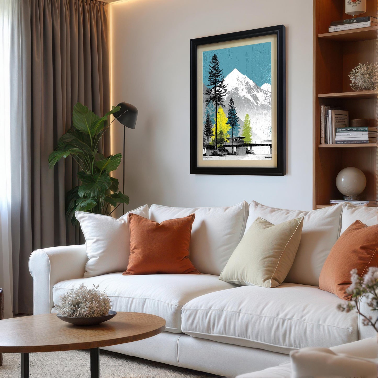 Black framed mountain landscape art print with an ivory mount, styled above a modern white sofa with orange cushions in a bright living room.