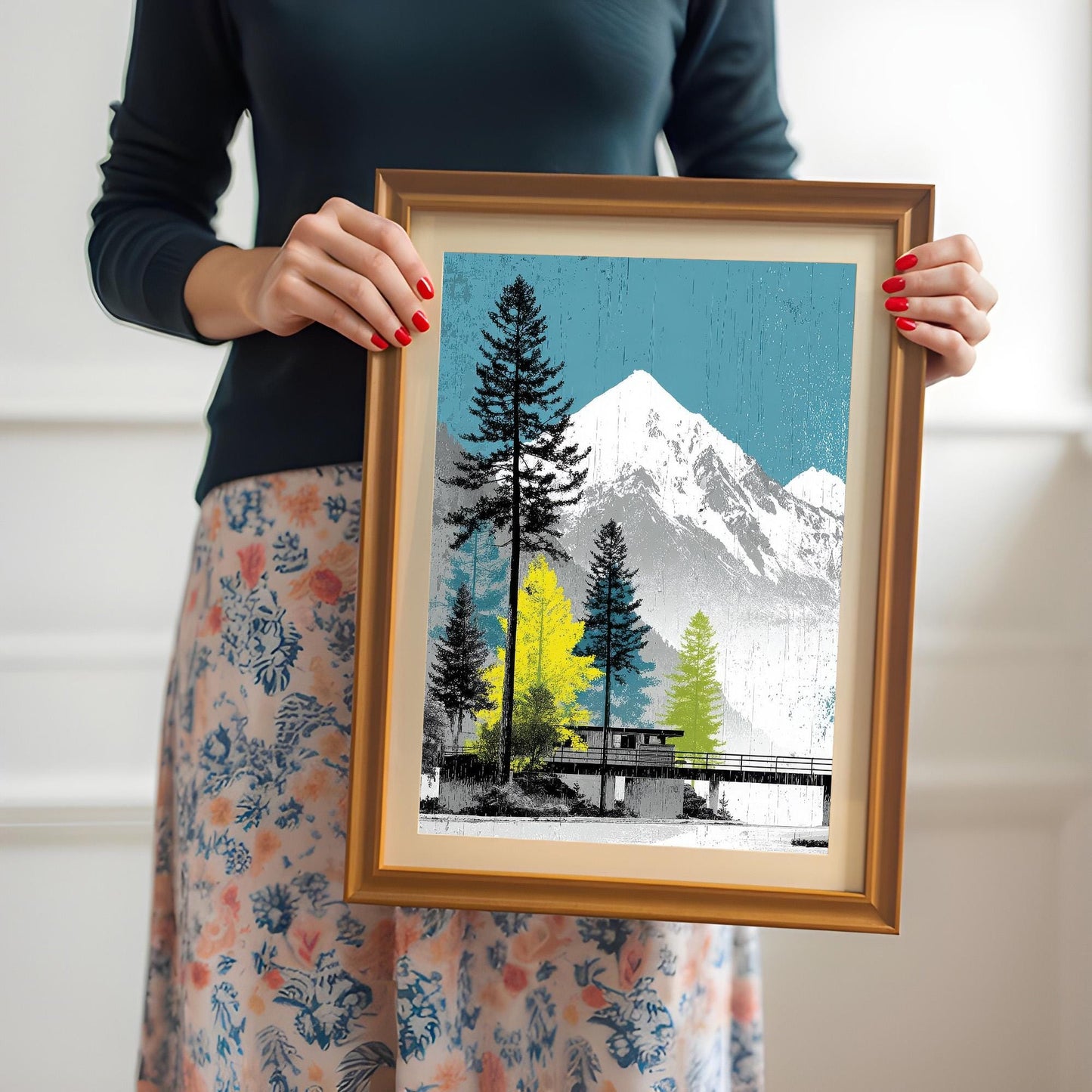 A woman holding an orange-framed mountain art print with an ivory mount to demonstrate the physical scale and quality of the finished product.