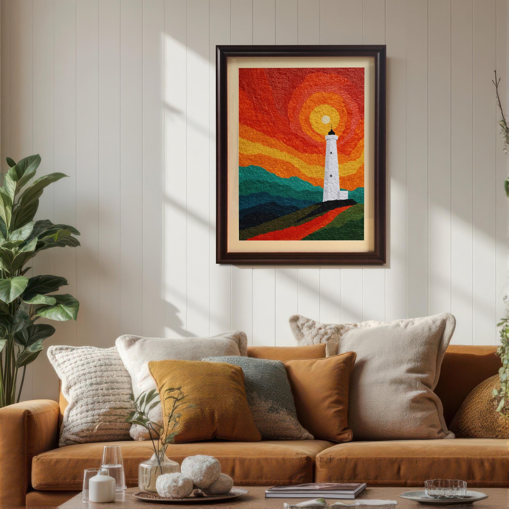 A coffee-framed lighthouse art print with a cream mount, hanging on a white paneled wall above a modern tan sofa decorated with various textured throw pillows.