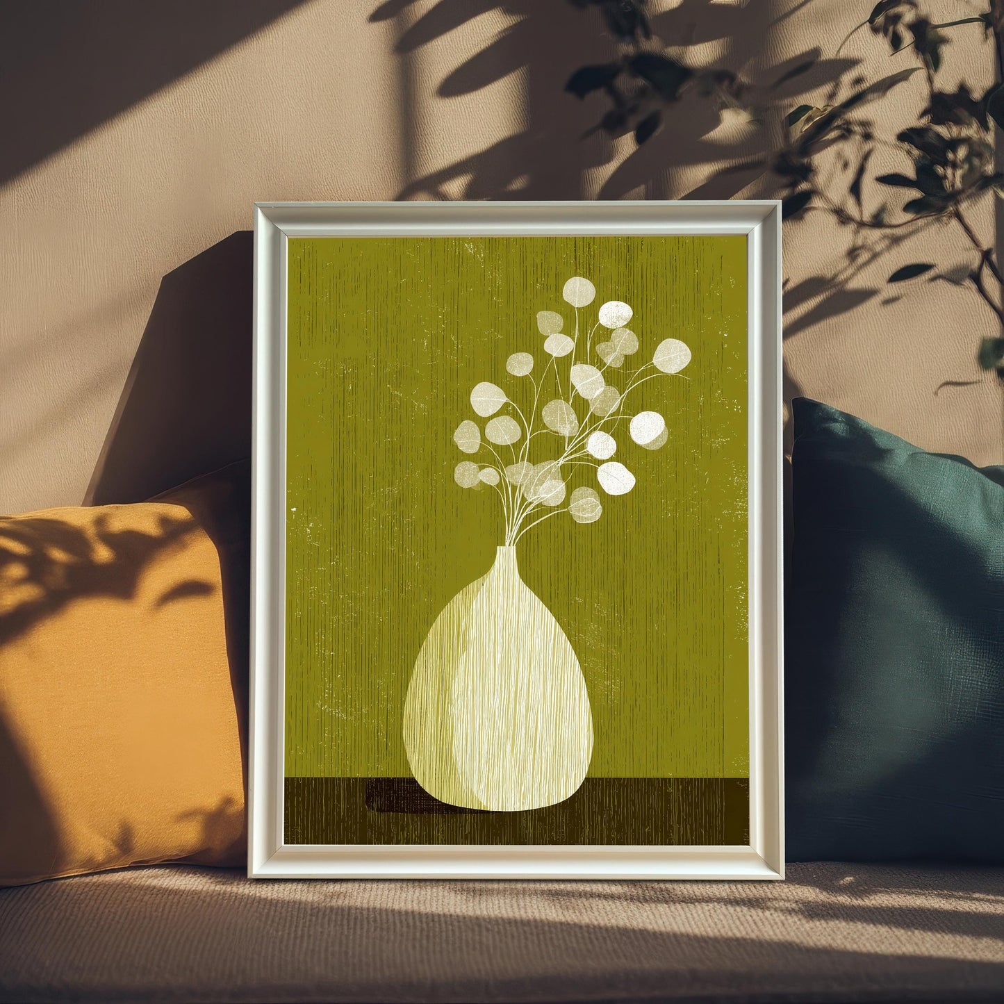 Minimalist botanical art print featuring a white vase with eucalyptus-style leaves on a moss green background, displayed in a white wooden frame leaning against a wall with soft sunlight shadows.