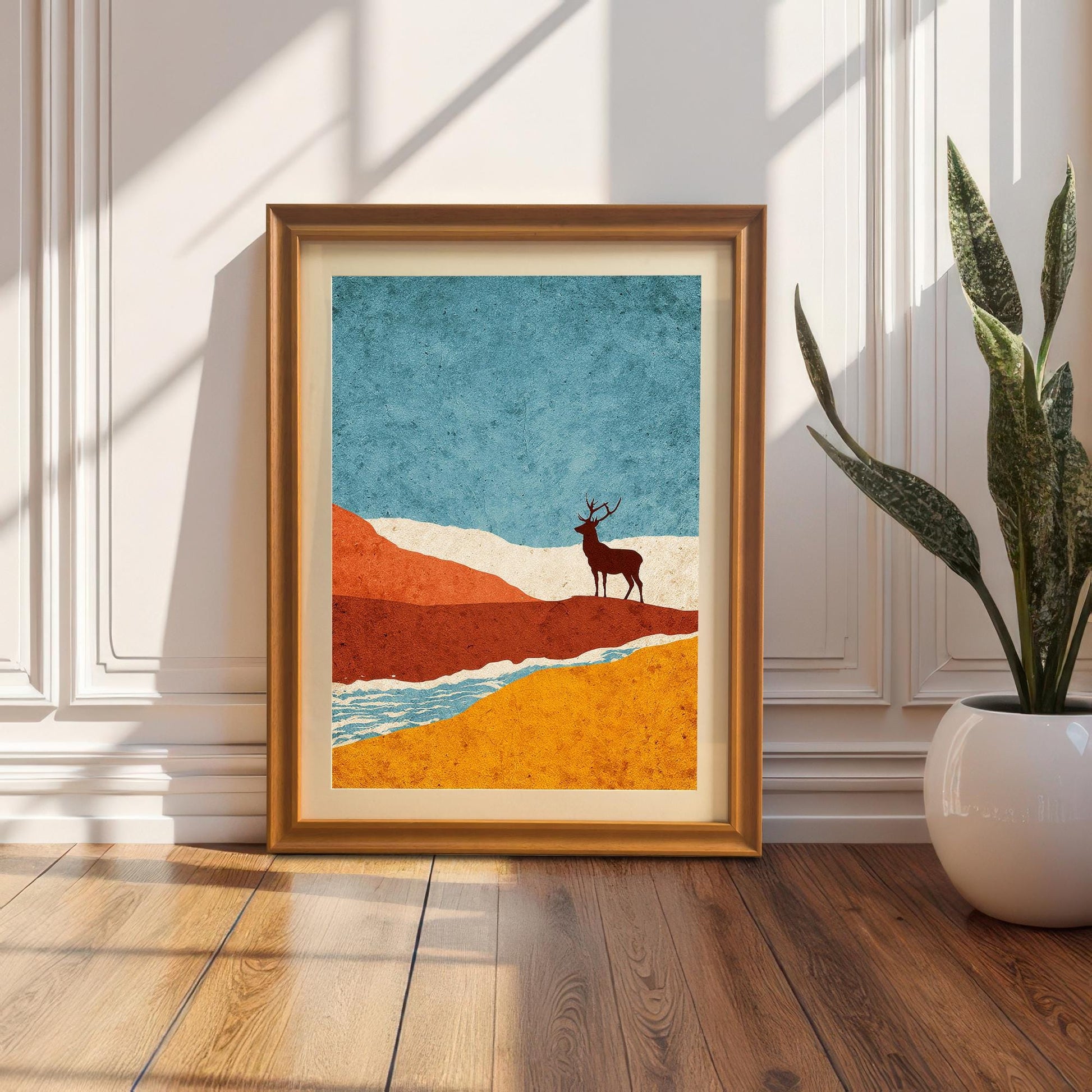 The orange-framed art print with a cream mount resting on a light wood floor against a white wall, illuminated by soft natural sunlight.