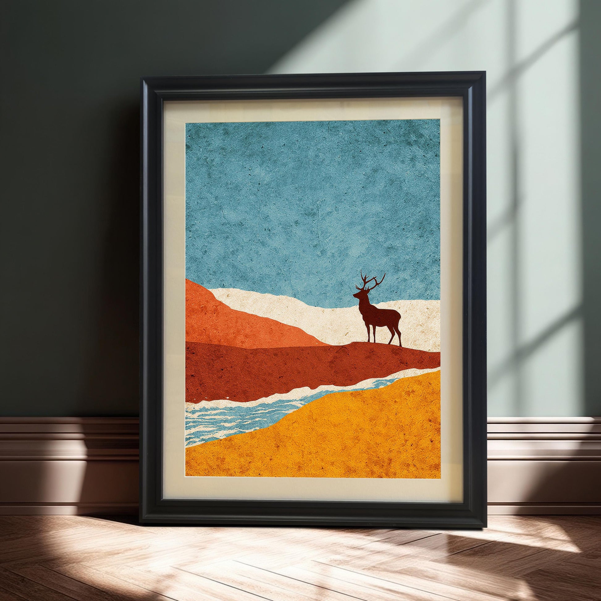 A black-framed stag art print with a cream mat, leaning against a dark sage green wall on a light herringbone wood floor, captured in dramatic natural sunlight and shadow.