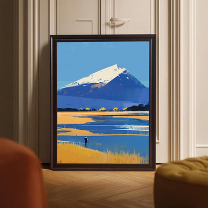 A framed art print of a blue and gold mountain landscape resting on a light-colored herringbone wood floor. The dark wood frame is positioned in front of a white paneled door, with soft-focus furniture appearing in the bottom corners of the frame.