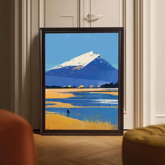 A framed art print of a blue and gold mountain landscape resting on a light-colored herringbone wood floor. The dark wood frame is positioned in front of a white paneled door, with soft-focus furniture appearing in the bottom corners of the frame.