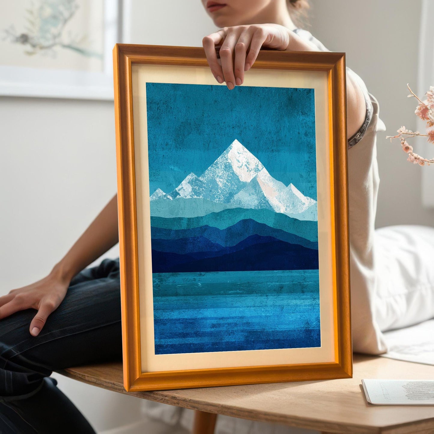 A lifestyle shot of a person holding an orange wood framed mountain print with a white mount. This photo provides a sense of scale and shows the natural grain of the wood frame in a home setting.