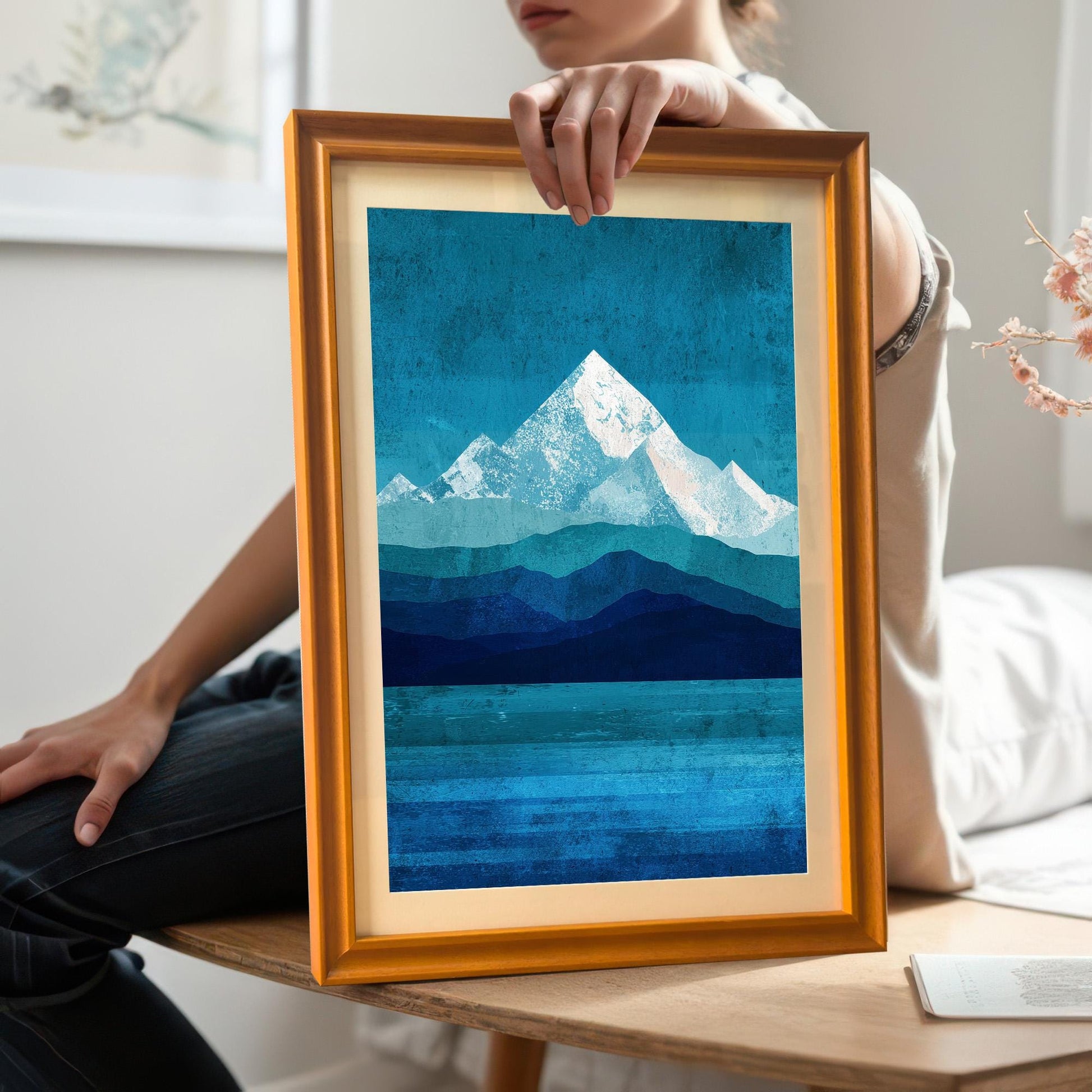 A lifestyle shot of a person holding an orange wood framed mountain print with a white mount. This photo provides a sense of scale and shows the natural grain of the wood frame in a home setting.