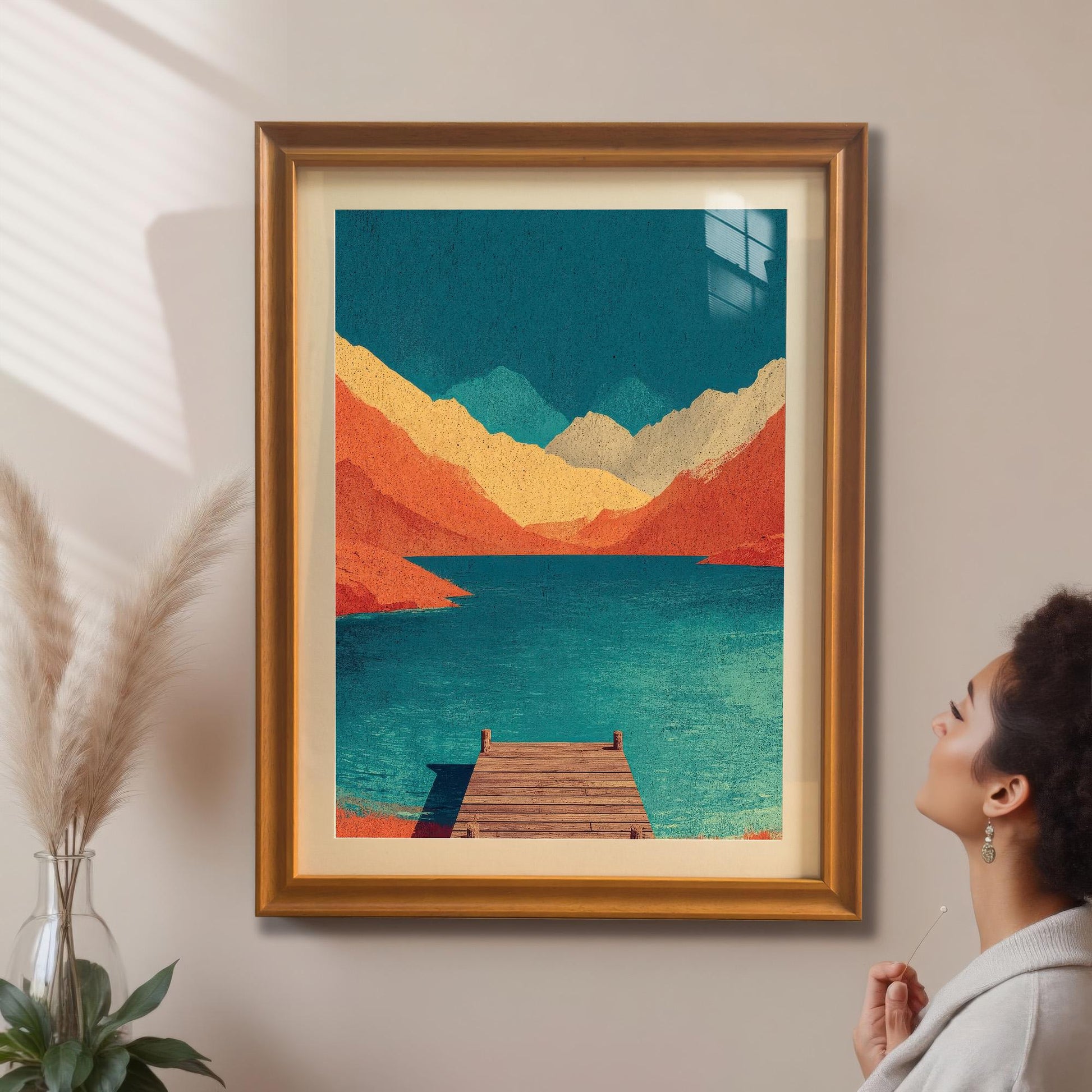 A woman admiring a large, honey-colored wood framed mountain landscape print hanging on a beige wall in a sunlit room.