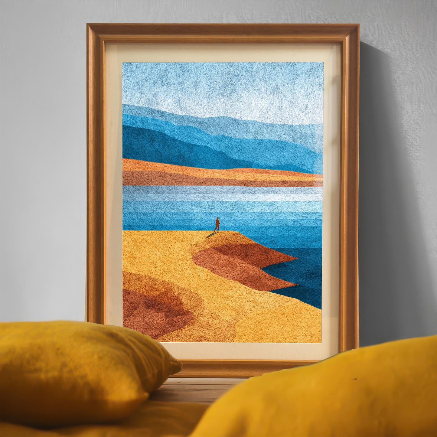 Close-up shot of the orange wood framed landscape art sitting behind yellow cushions, emphasizing the textured paper and warm interior decor vibe.