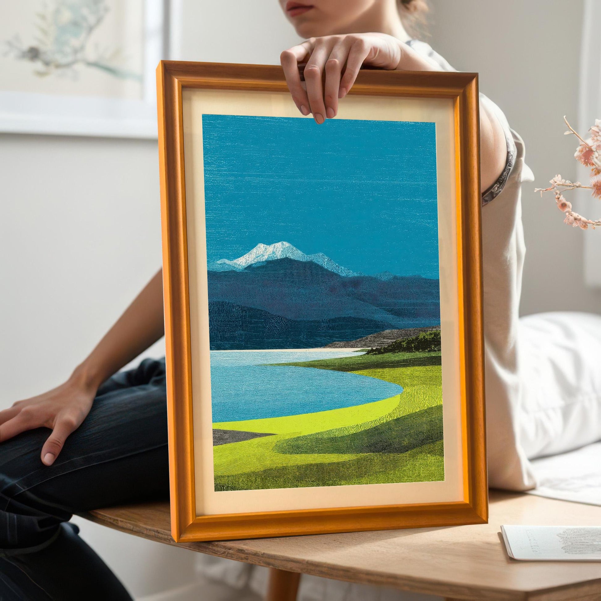 A person holding a medium-sized orange wood-framed art print with an off-white mount to show the scale and physical frame quality.