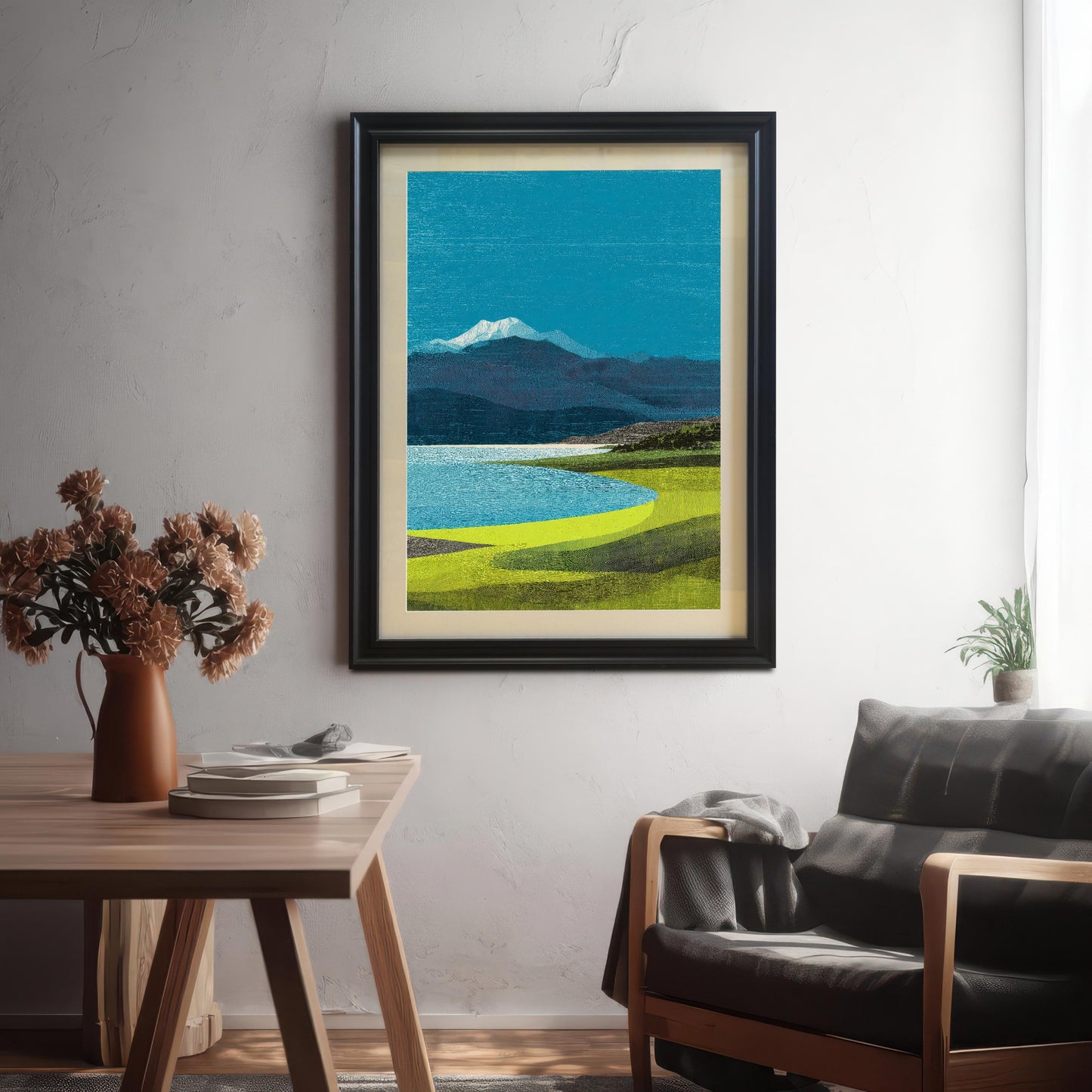 A black-framed mountain landscape print with an off-white mat board mounted on a white textured wall in a modern living room setting.