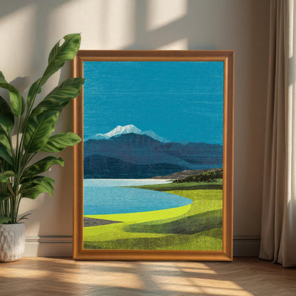 Large orange-toned wood-framed mountain landscape print leaning on a floor next to a large green leafy plant in a sunlit room.