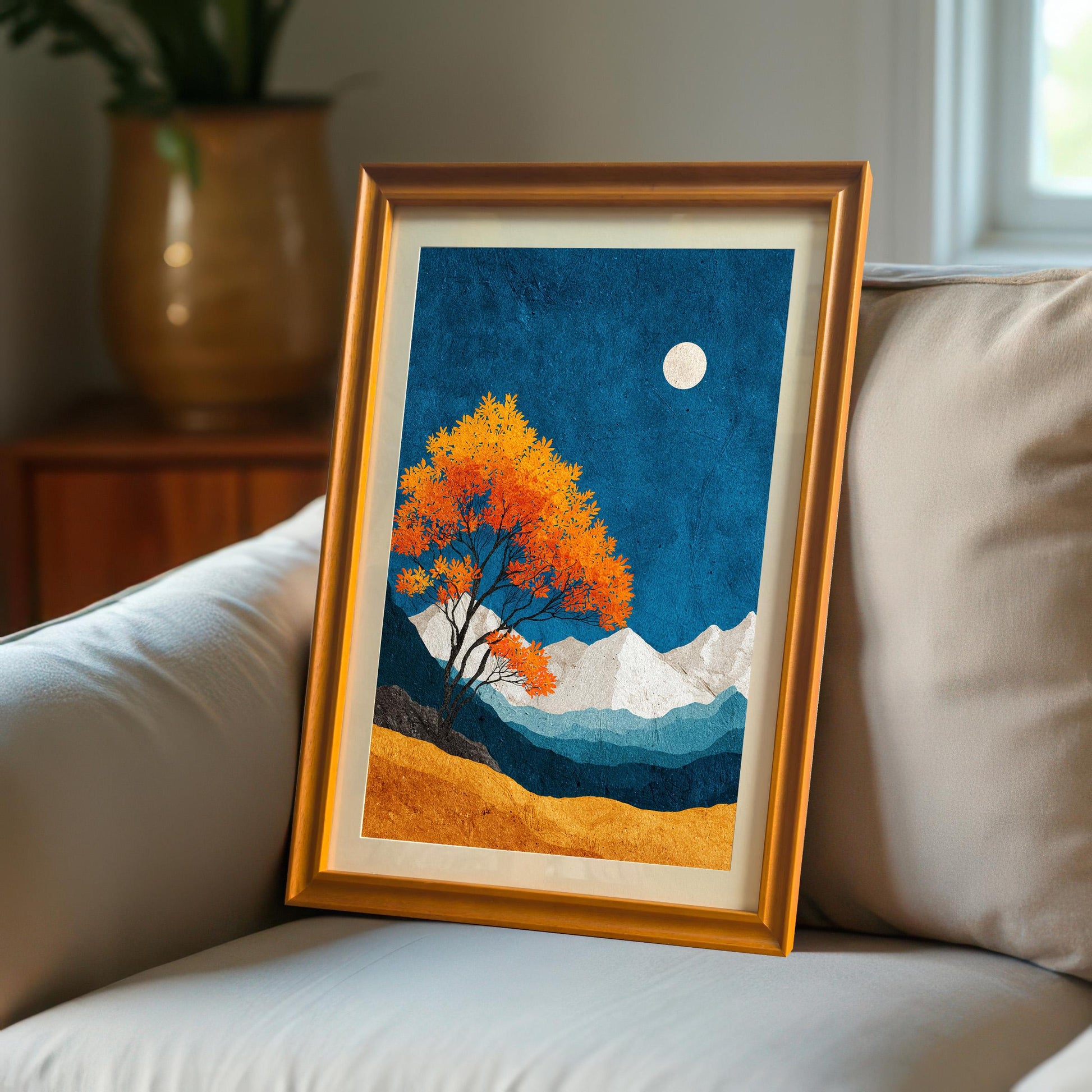 A framed art print with an orange wood frame leaning against a soft grey sofa in a cozy, sunlit living room setting.