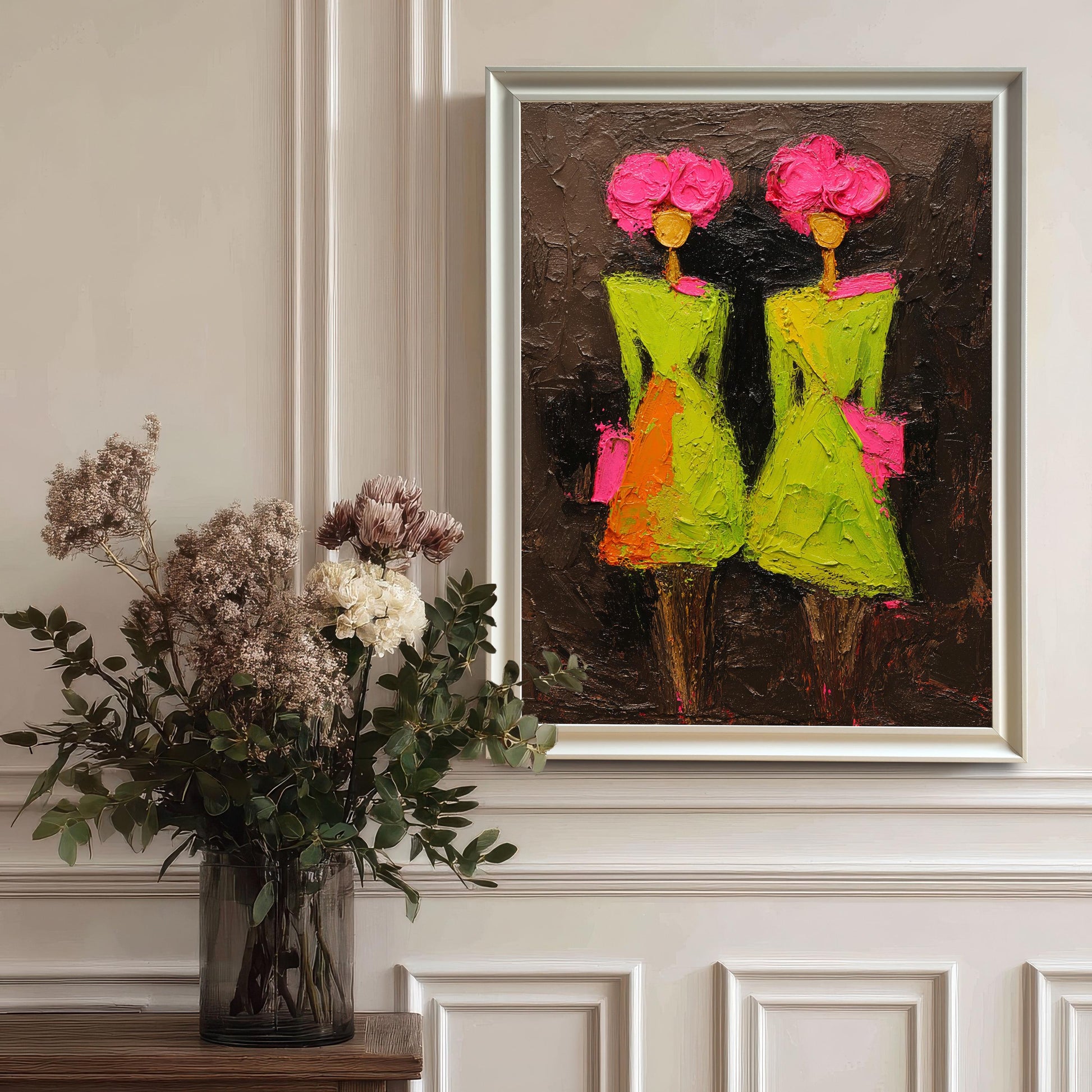 The colorful abstract artwork presented in a sleek white frame, hanging on a white wall with classic molding details above a dark wood table featuring a large glass vase of dried floral arrangements.