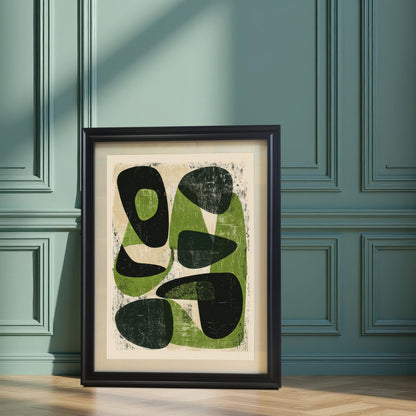 A large, black-framed abstract art print featuring mid-century modern organic shapes in sage green and black, leaning against a decorative teal paneled wall on a herringbone wood floor.