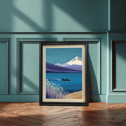 A vertical black wood framed art print featuring a serene mountain and lake landscape leaning against a teal wainscoted wall on a herringbone wood floor. The print includes a cream-colored mount.