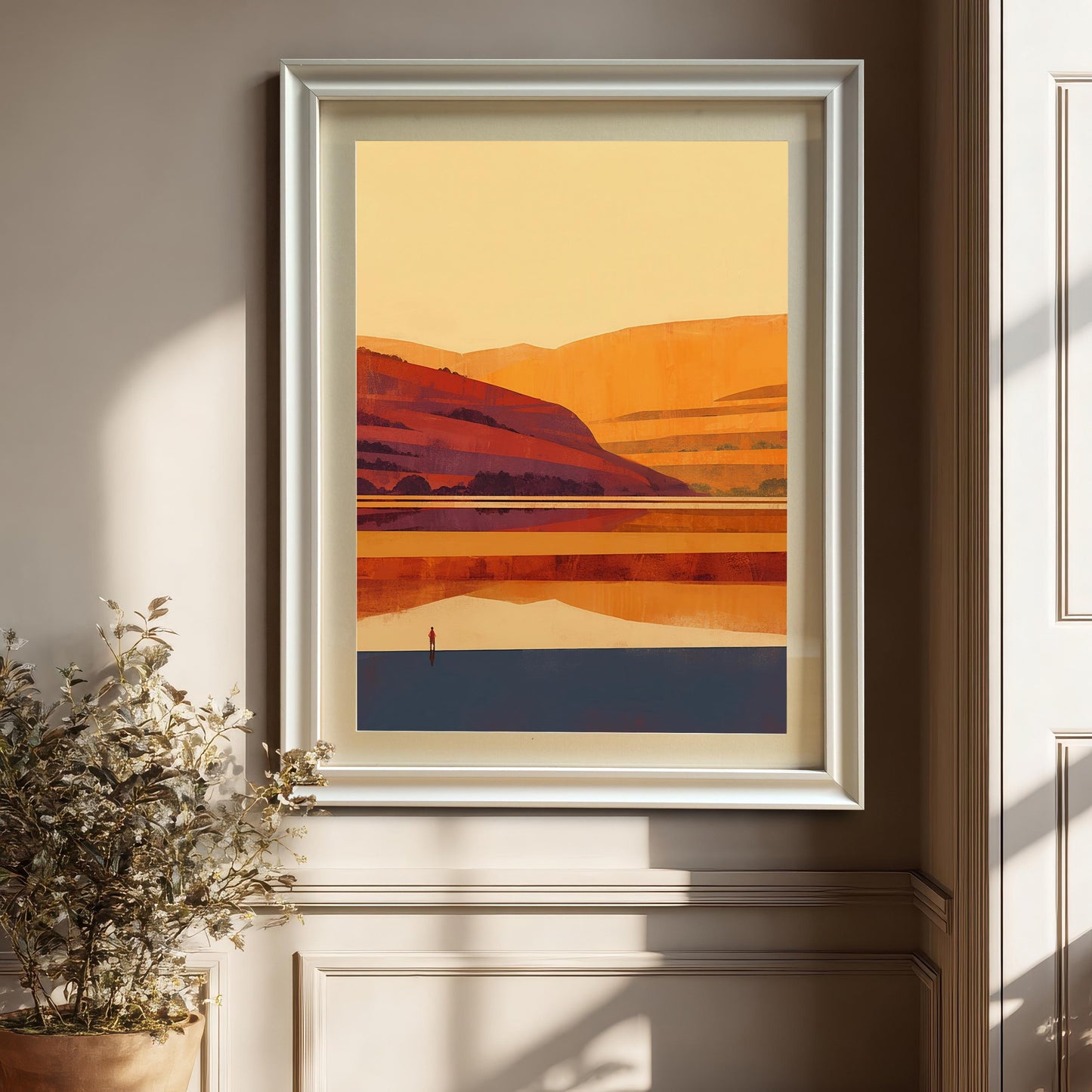 Close-up of a white wood-framed landscape art print hanging on a beige wall with natural sunlight and shadows, featuring a white mount.