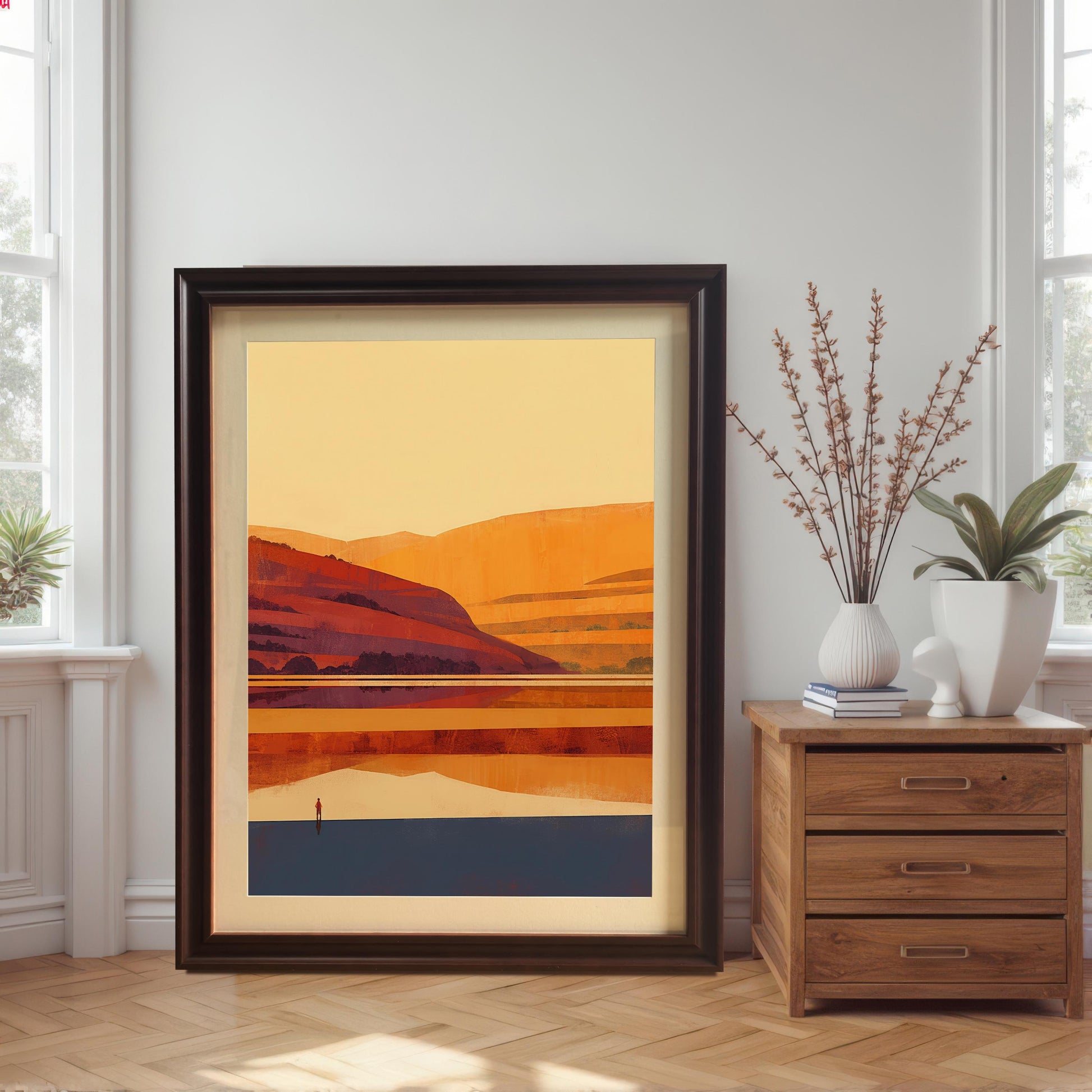Large coffee-colored wood frame with a cream mount leaning against a white wall on a herringbone wood floor, situated next to a wooden side table with plants.