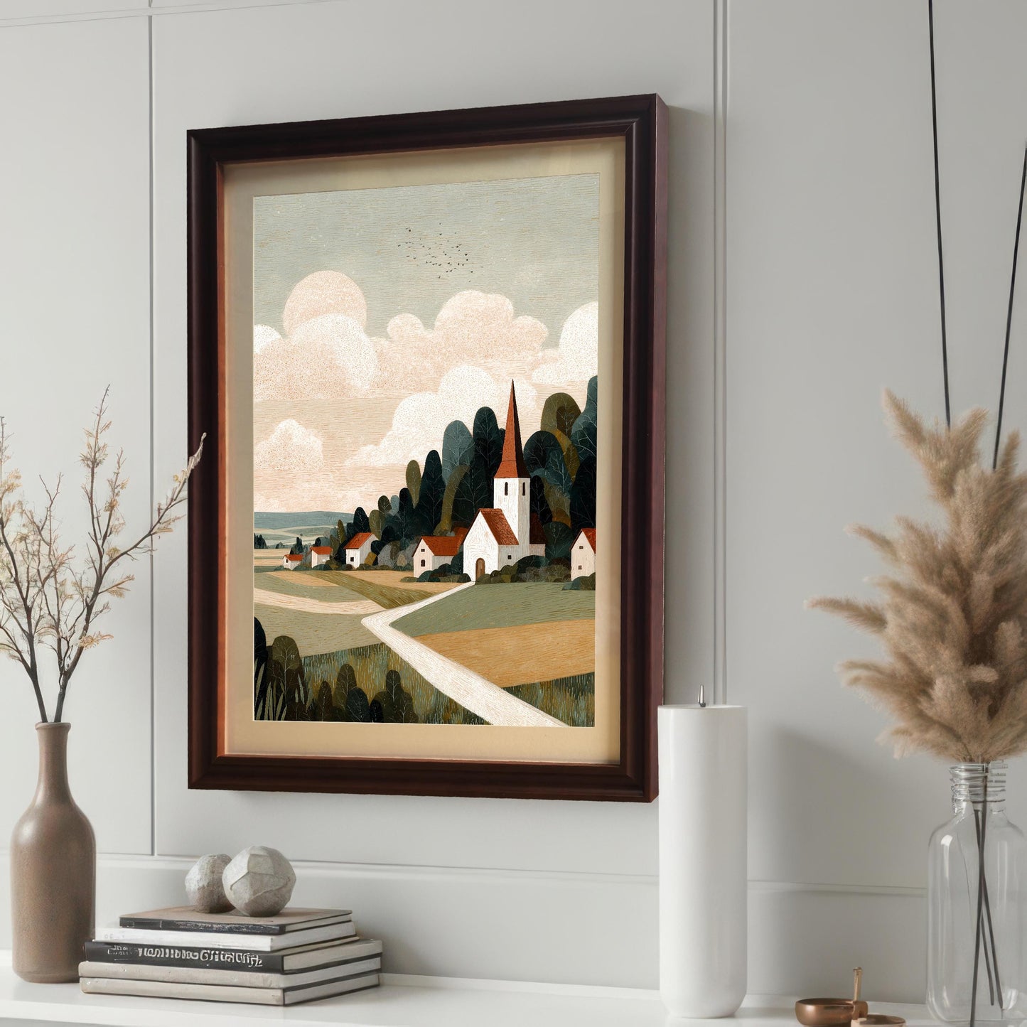 A close-up side view of the framed landscape artwork in a coffee-colored frame with a mat, displayed on a white shelf next to books, a white candle, and dried pampas grass.