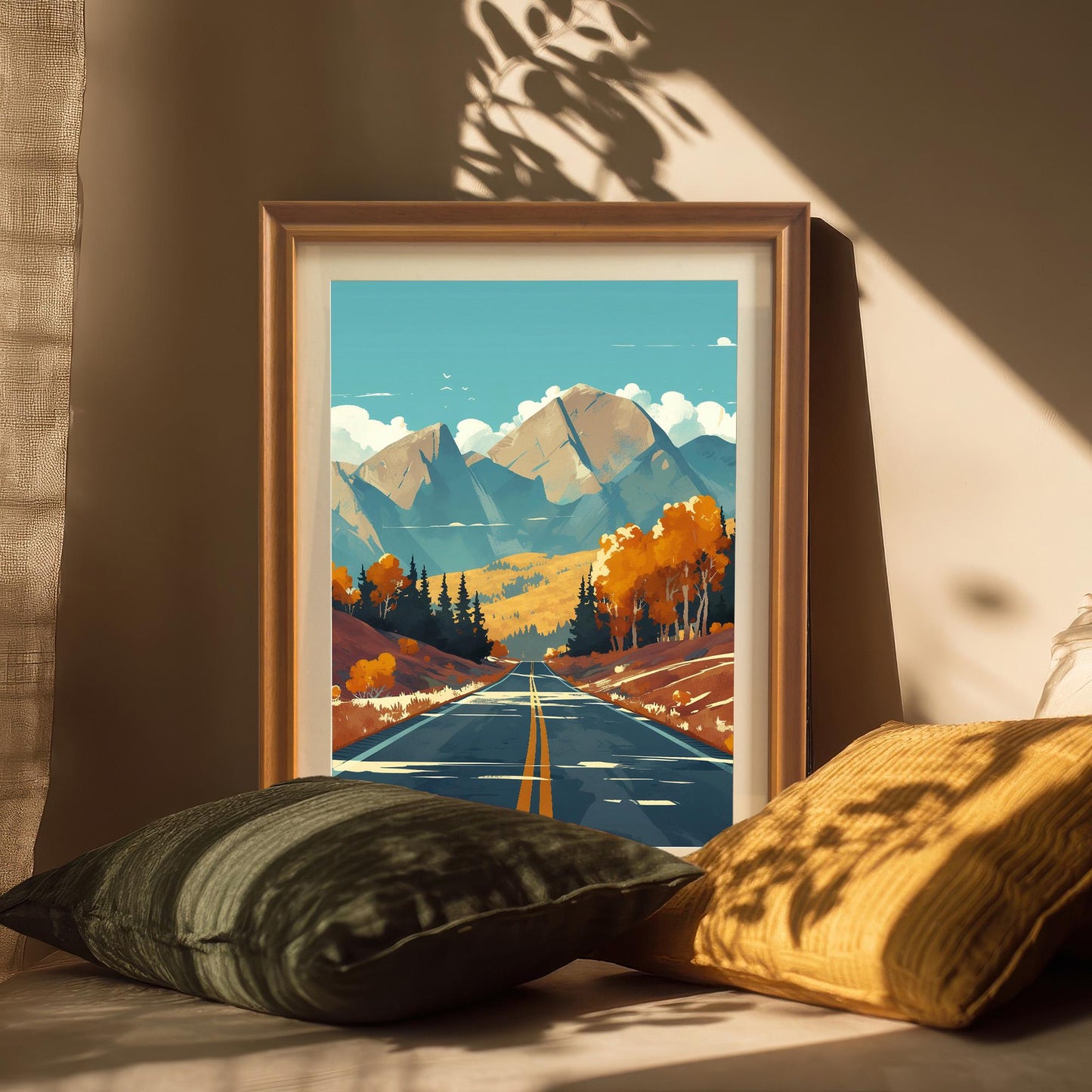 Framed autumn scenery art print with a white mount, resting on a surface with soft pillows in warm, natural sunlight.