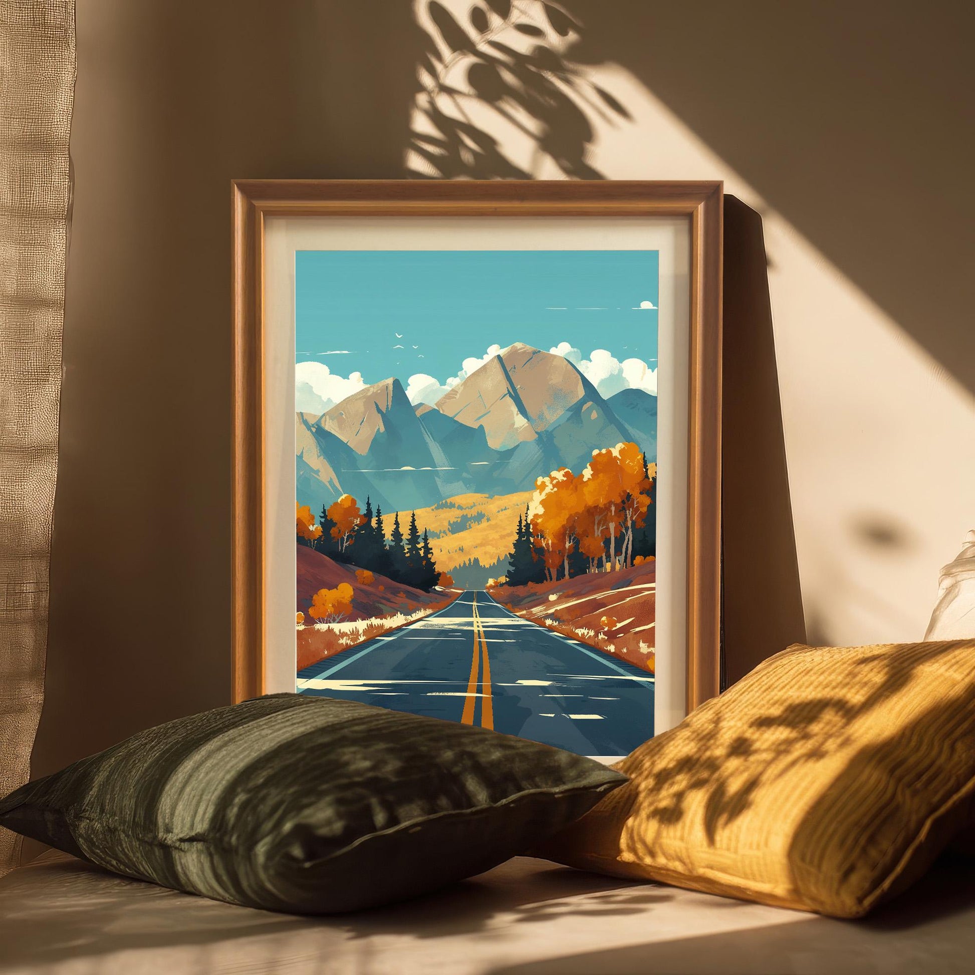 Framed autumn scenery art print with a white mount, resting on a surface with soft pillows in warm, natural sunlight.