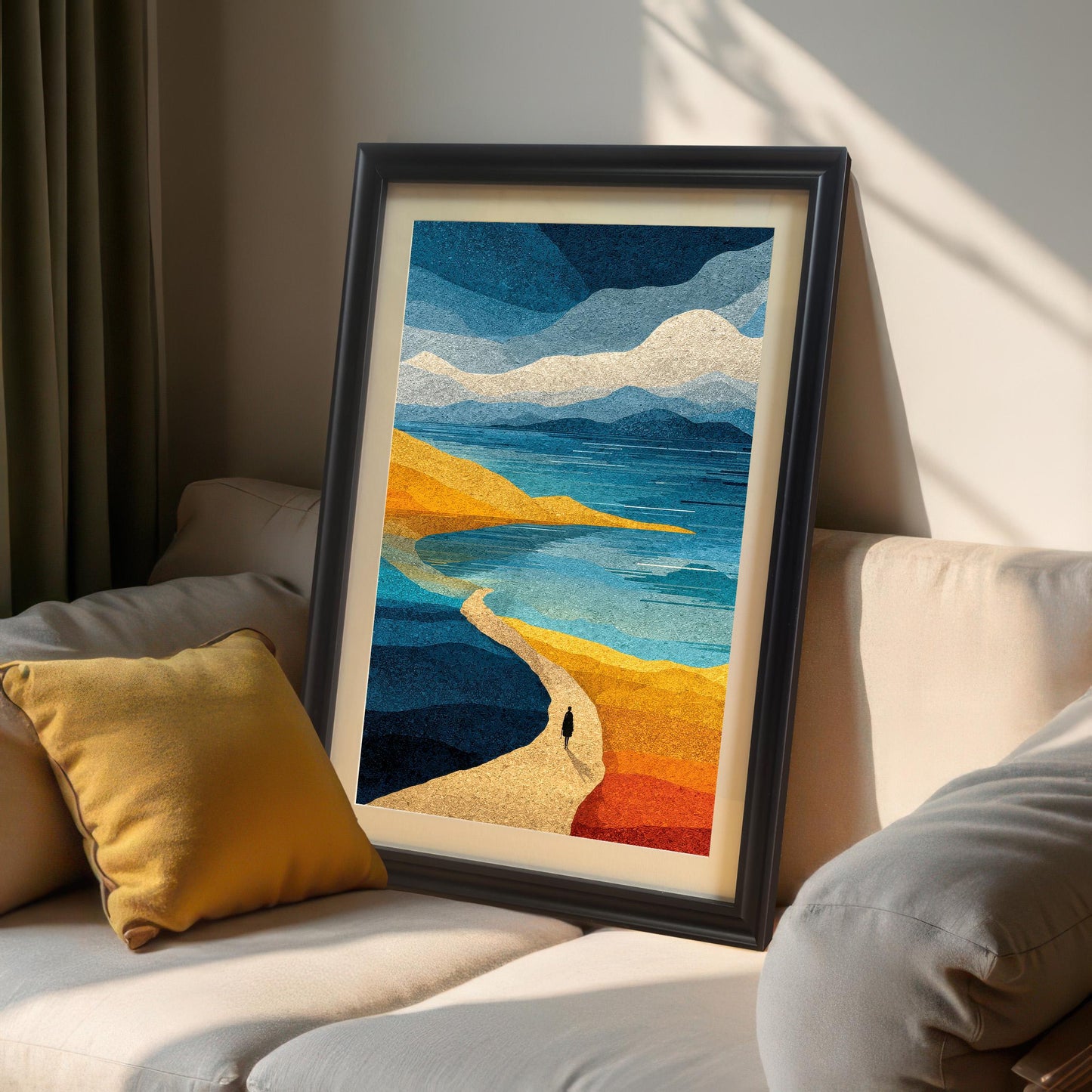 A black wood framed abstract art print with a white mount leaning on a neutral-toned sofa in a sunlit room with a yellow accent pillow.
