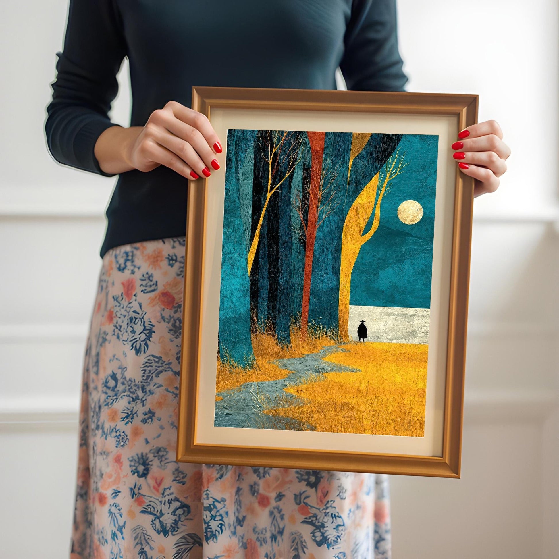 A person holding the medium-sized framed art print to show scale, featuring the orange wood frame and an off-white mount.