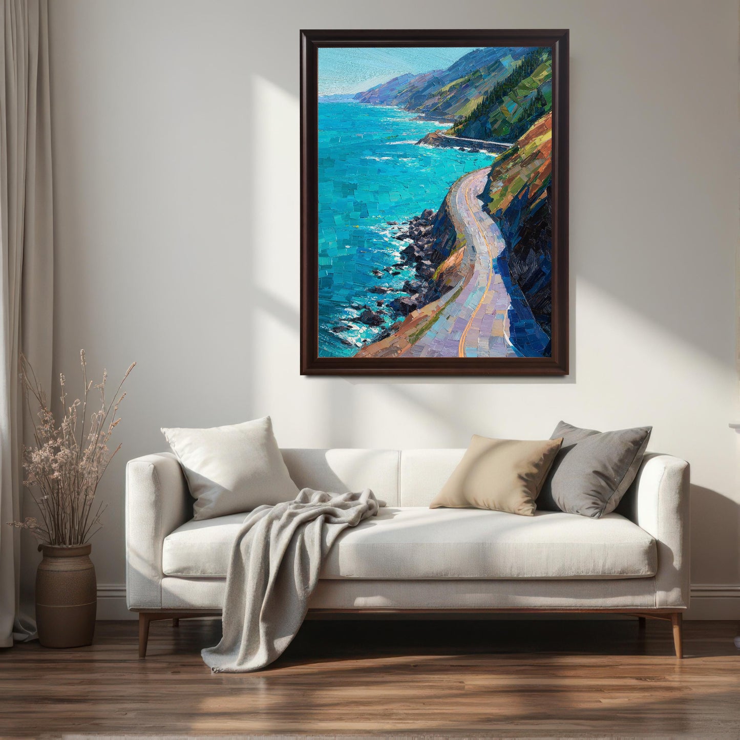 A coffee brown wood framed large landscape painting of a winding cliffside road, hanging above a contemporary white sofa with neutral-toned throw pillows in a sunlit living room.