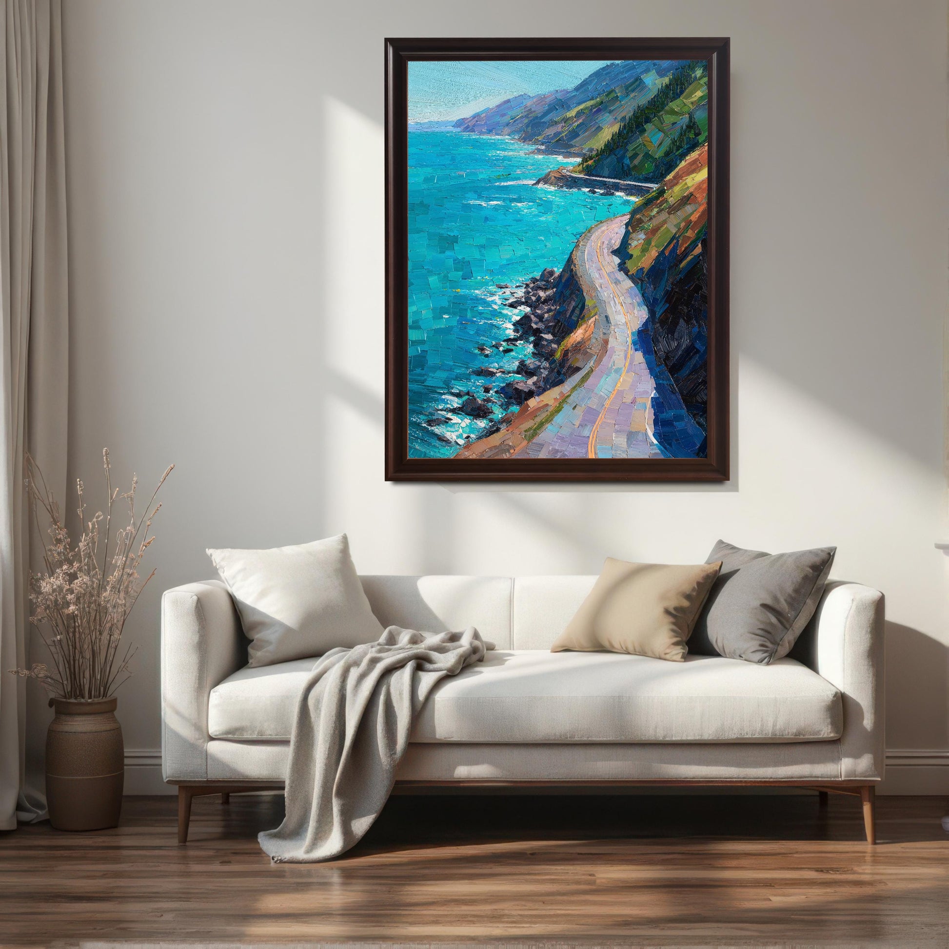 A coffee brown wood framed large landscape painting of a winding cliffside road, hanging above a contemporary white sofa with neutral-toned throw pillows in a sunlit living room.