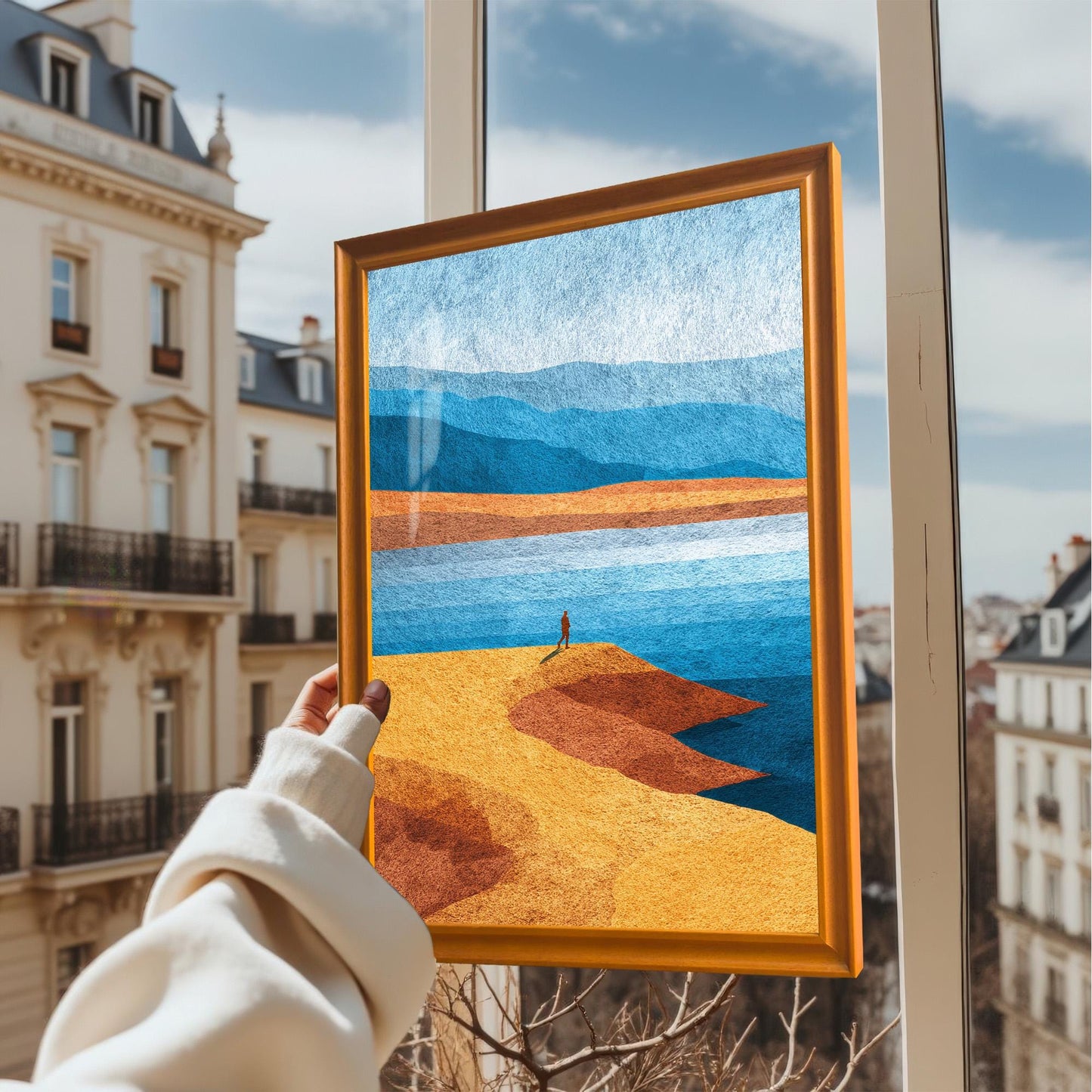 A hand holding the orange wood framed art print against a window with a blurred European city background, showing the vibrant colors in natural light.