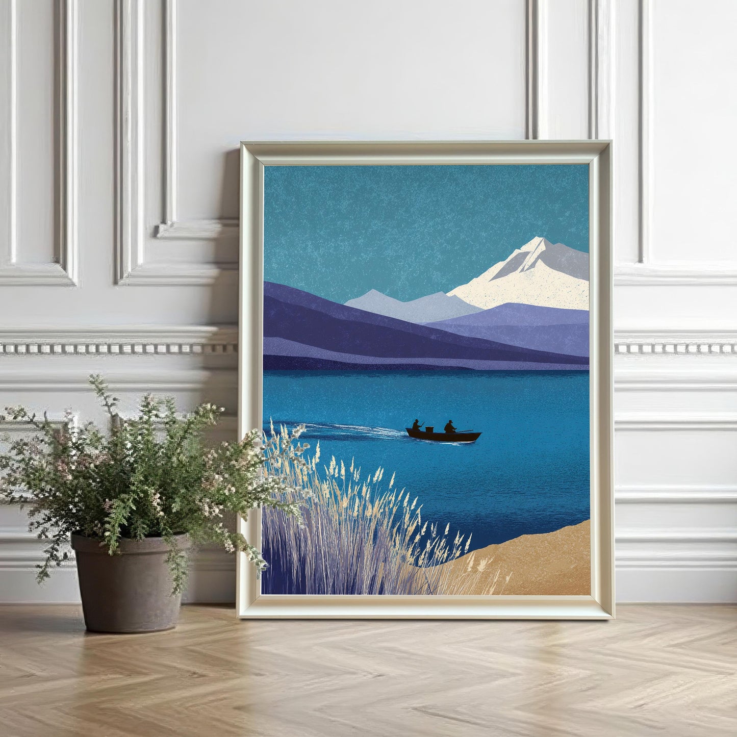 A large white wood framed art print without a mount, resting on a light wood floor next to a potted plant against a classic white decorative wall.